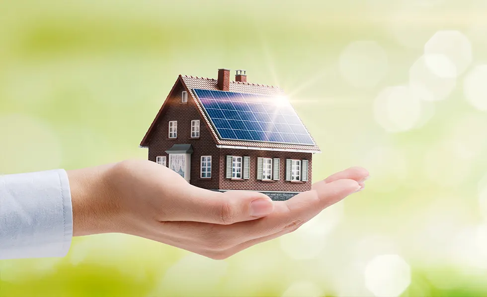 A hand holding a model house with solar panels on the roof, symbolizing sustainable energy and solar power incentives