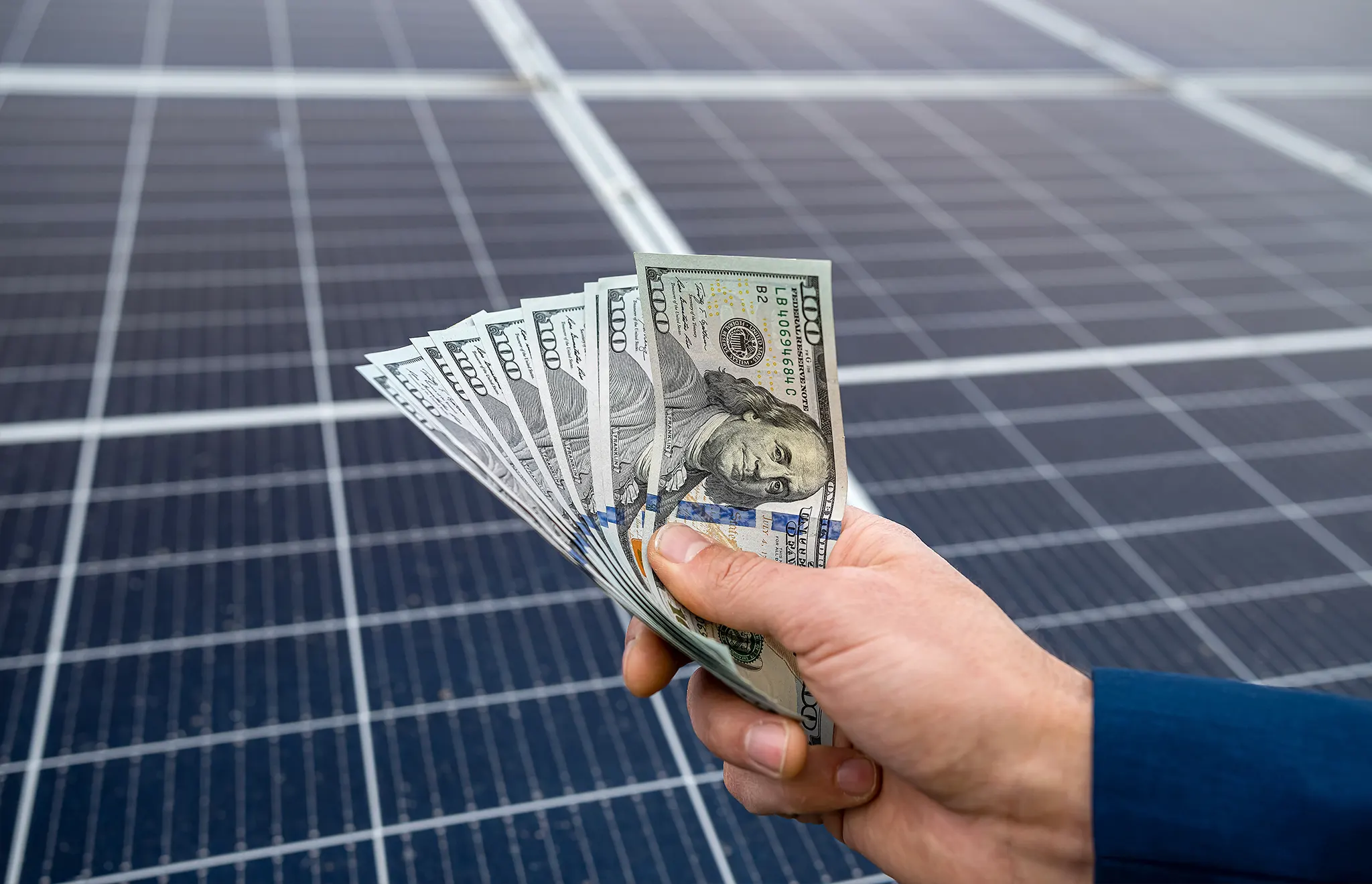 Hand Holding Money in Front of Solar Panels